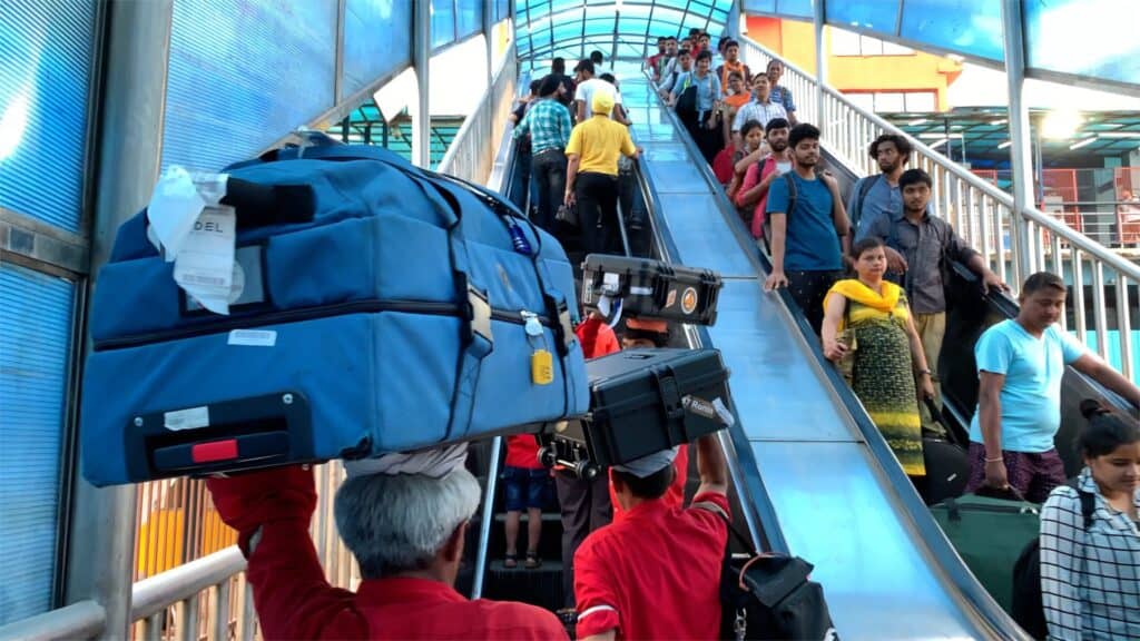 Überfüllte Rolltreppe an einem Flughafen, Gepäckträger tragen Gepäck über den Köpfen.