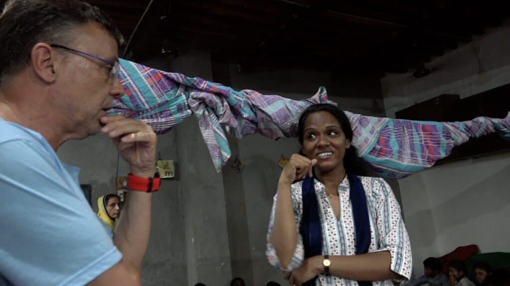 Mann und Frau diskutieren, über ihnen bunter Stoff, möglicherweise während eines Workshops oder Unterrichts.