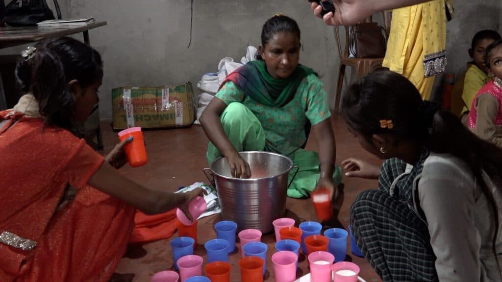 Frauen gießen in einer ländlichen Gemeinde Milch in Tassen für Kinder.