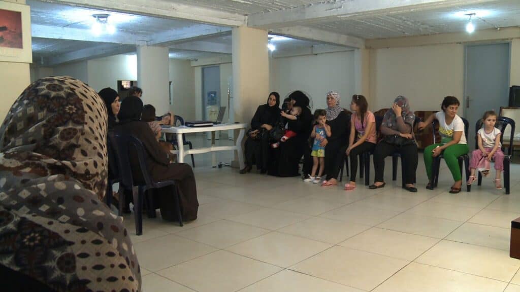 Eine Gruppe von Frauen und Kindern sitzt in einem Raum, einige tragen Kopftücher.