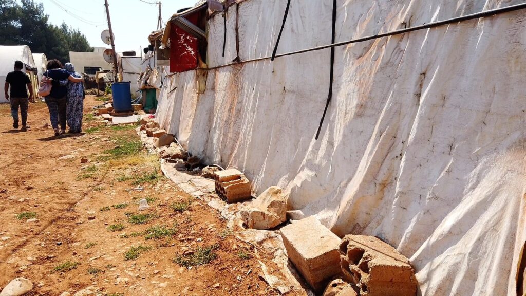 Bewohner eines Flüchtlingslagers gehen an provisorischen Unterkünften aus Stoff und Betonblöcken vorbei.