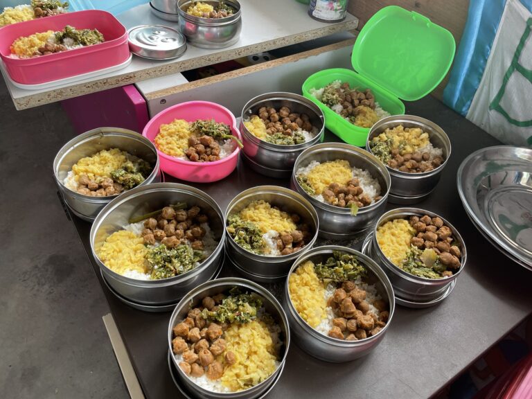 Mehrere Edelstahlbehälter, gefüllt mit Reis, Dal und Soja-Nuggets, bereit zur Verteilung.