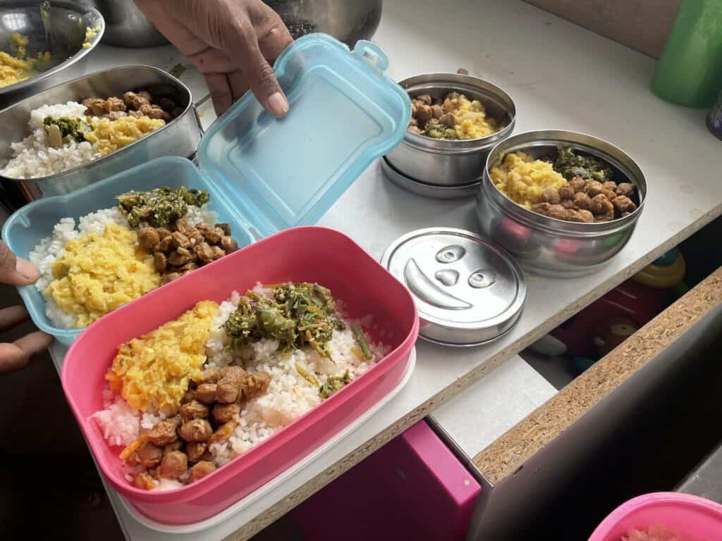 Hände packen gesunde vegetarische Lunchboxen mit Reis, Dal und Gemüse.