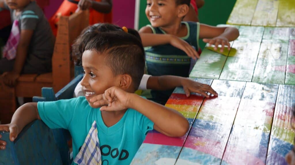 Glückliche Kinder sitzen an einem bunten Tisch in einem Klassenzimmer.
