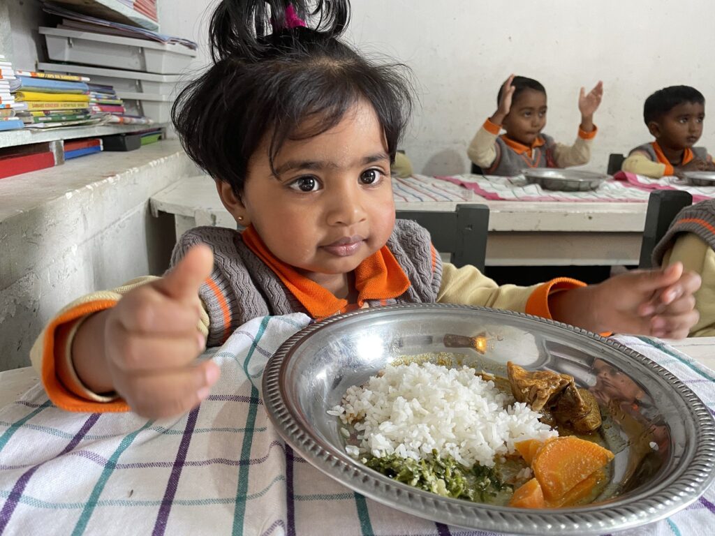 Ein junges Mädchen genießt bei einem Schulspeisungsprogramm eine nahrhafte Mahlzeit aus Reis, Gemüse und Curry.