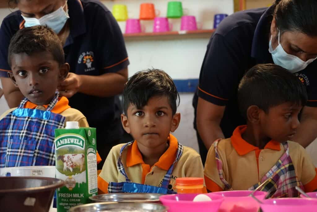 Sri-lankische Kinder in Schürzen backen mit Milch und nehmen an einem Programm von Child Action Lanka teil.