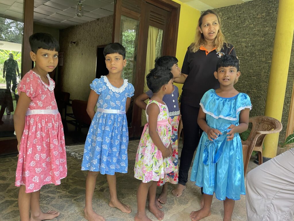 Gruppe von Kindern in Kleidern, mit einer Frau, möglicherweise einer Lehrerin oder Betreuerin.