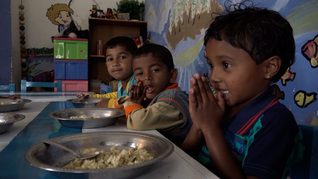 Vier Kinder sitzen an einem Tisch und essen. Sie scheinen in einer Kindertagesstätte oder Schule zu sein.