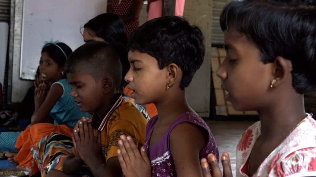 Kinder beten mit gefalteten Händen vor dem Essen.