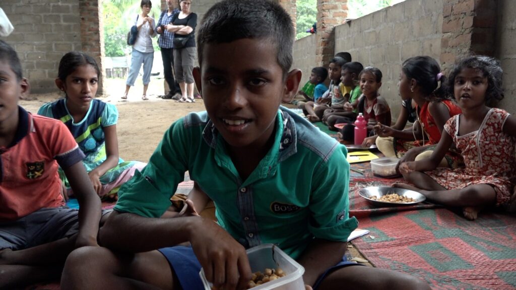 Lächelnder Junge isst mit anderen Kindern in Sri Lanka einen Snack.