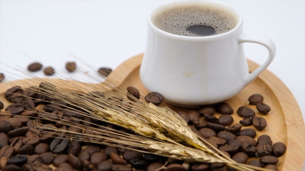Eine Tasse schwarzen Kaffee steht mit Kaffeebohnen und Weizenhalmen auf einem Holztablett.