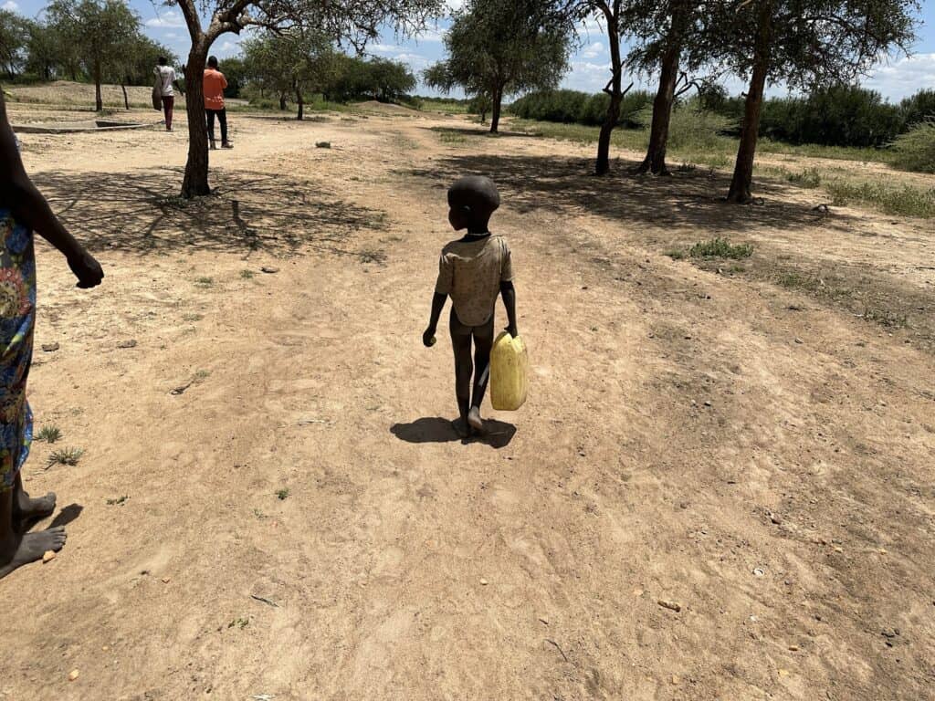 Kleines Kind trägt Wasser in trockener Landschaft