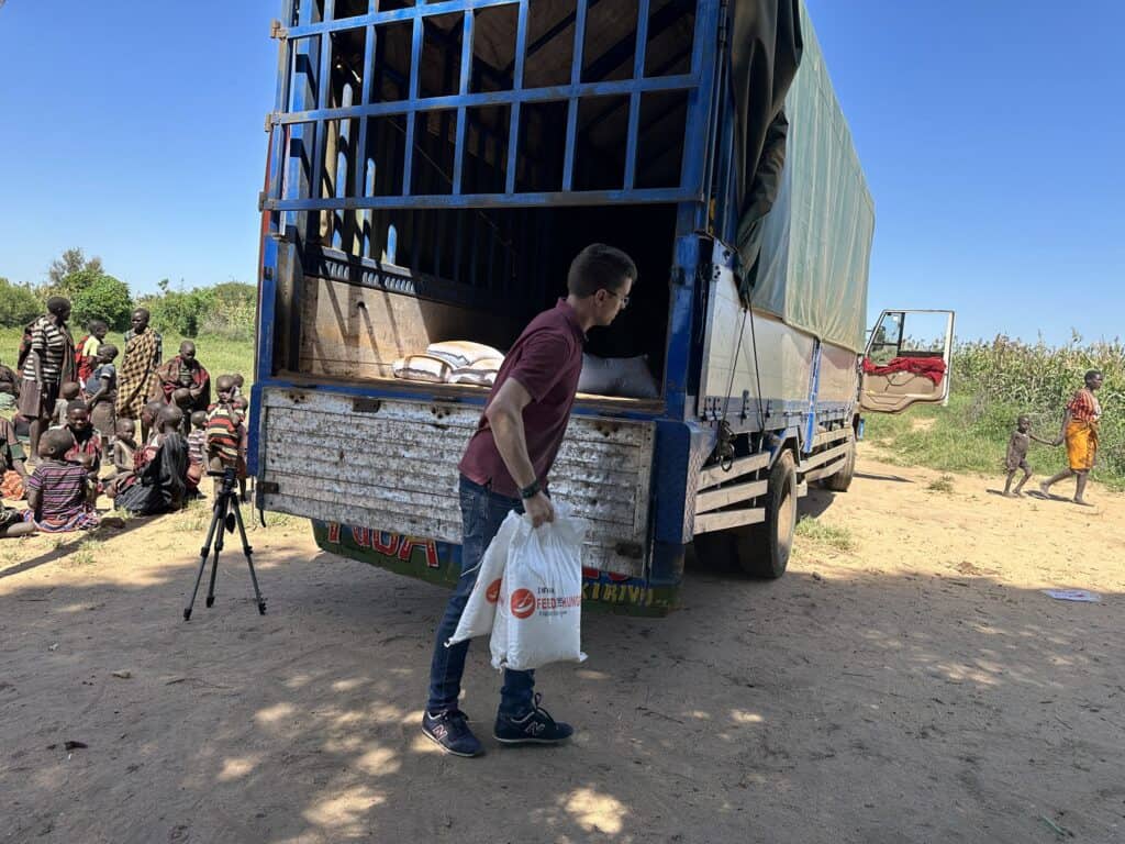 Ein Mann lädt Säcke mit Nahrungsmittelhilfe von einem Lastwagen für eine Gruppe von Menschen ab.