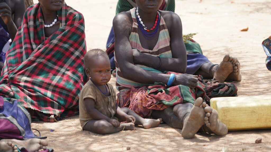 Afrikanische Frauen und Kinder sitzen auf dem Boden und tragen traditionelle Kleidung.