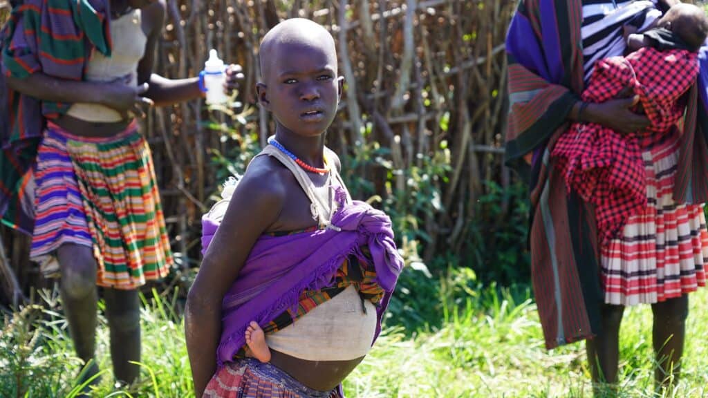Junges Mädchen in Afrika trägt ein Baby und trägt traditionelle Kleidung.