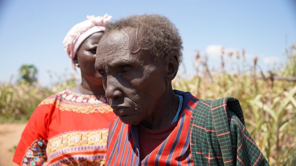 Älterer afrikanischer Mann und Frau in traditioneller Kleidung stehen auf einem Feld.