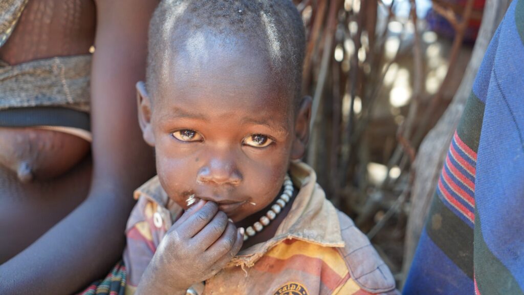Junges afrikanisches Kind mit Perlenkette, Blick in die Kamera.
