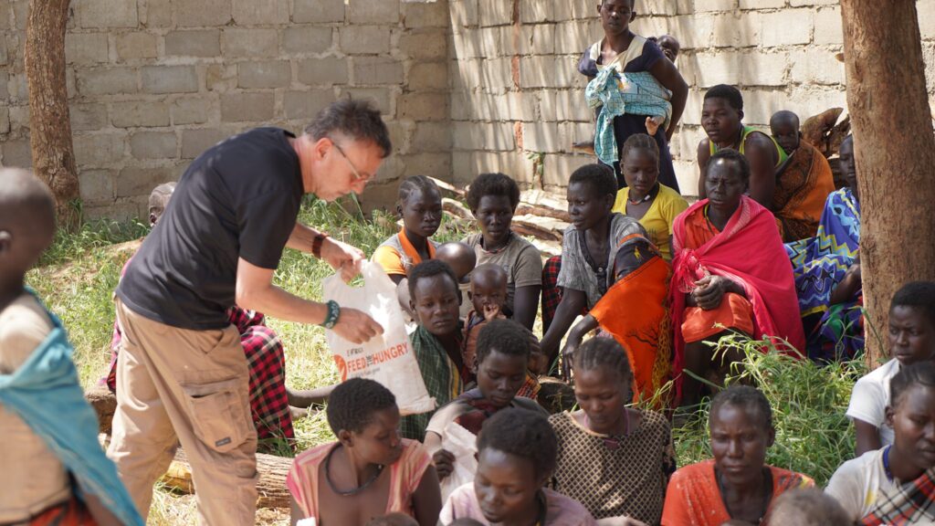 Mann verteilt Nahrungsmittelhilfe an hungrige Frauen und Kinder in Afrika. „Feed the Hungry“-Tasche sichtbar.