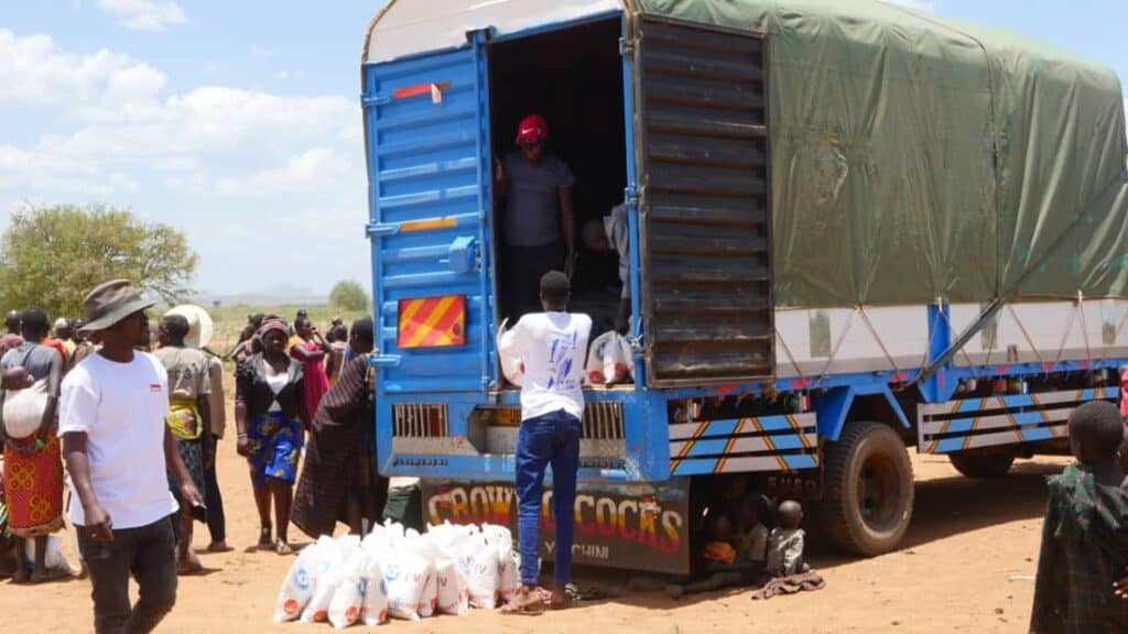 Nahrungsmittelhilfe im dürregeplagten Afrika. Freiwillige laden Getreidesäcke von einem Lastwagen vor einer Menschenmenge ab.