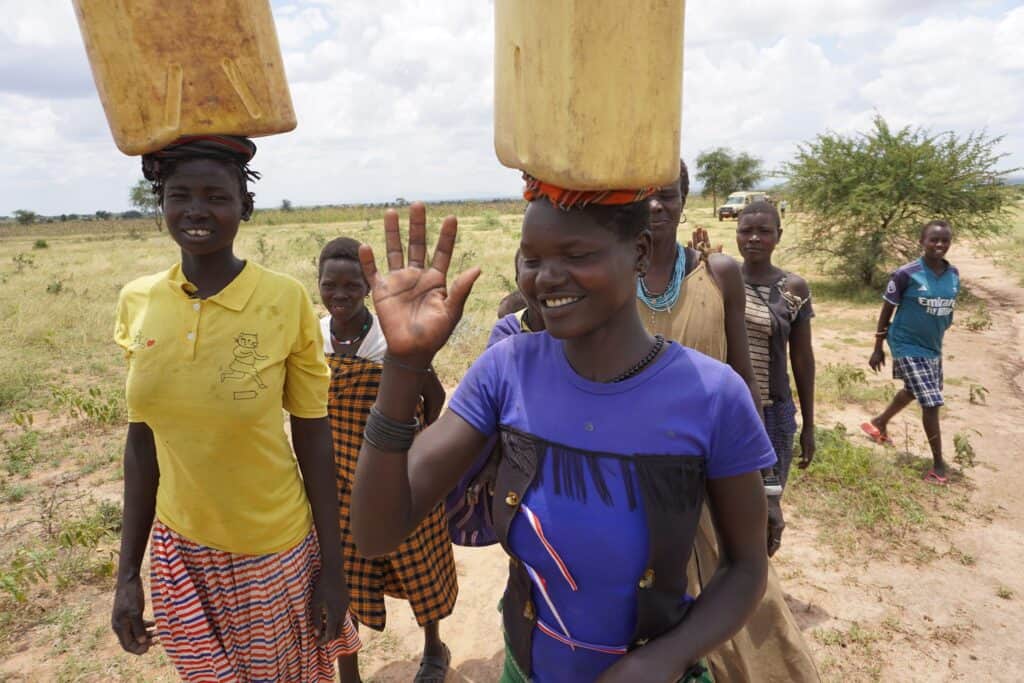 Afrikanische Frauen tragen Wasserbehälter und winken zur Begrüßung.