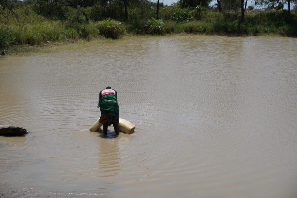 Frau füllt Wasserbehälter in einem ländlichen Teich