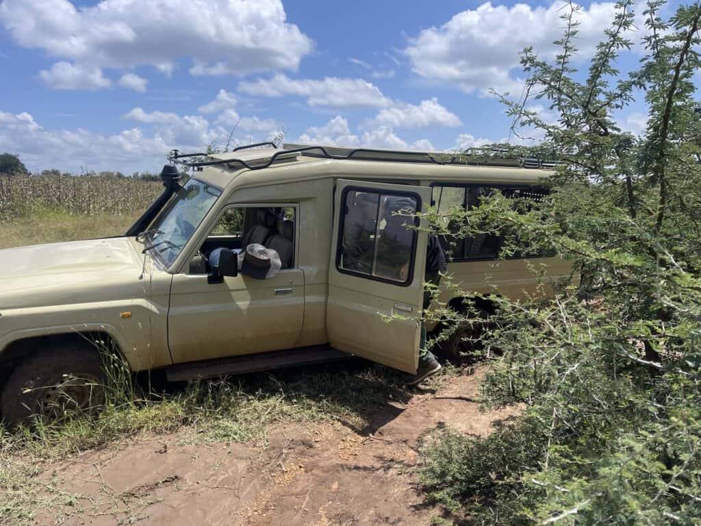 Safari-Tourfahrzeug steckt im Schlamm fest, Passagiere steigen aus.