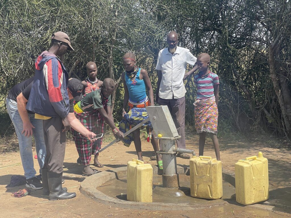 Gemeindemitglieder versammeln sich um eine neue Wasserpumpe und füllen Behälter. Zugang zu sauberem Wasser.
