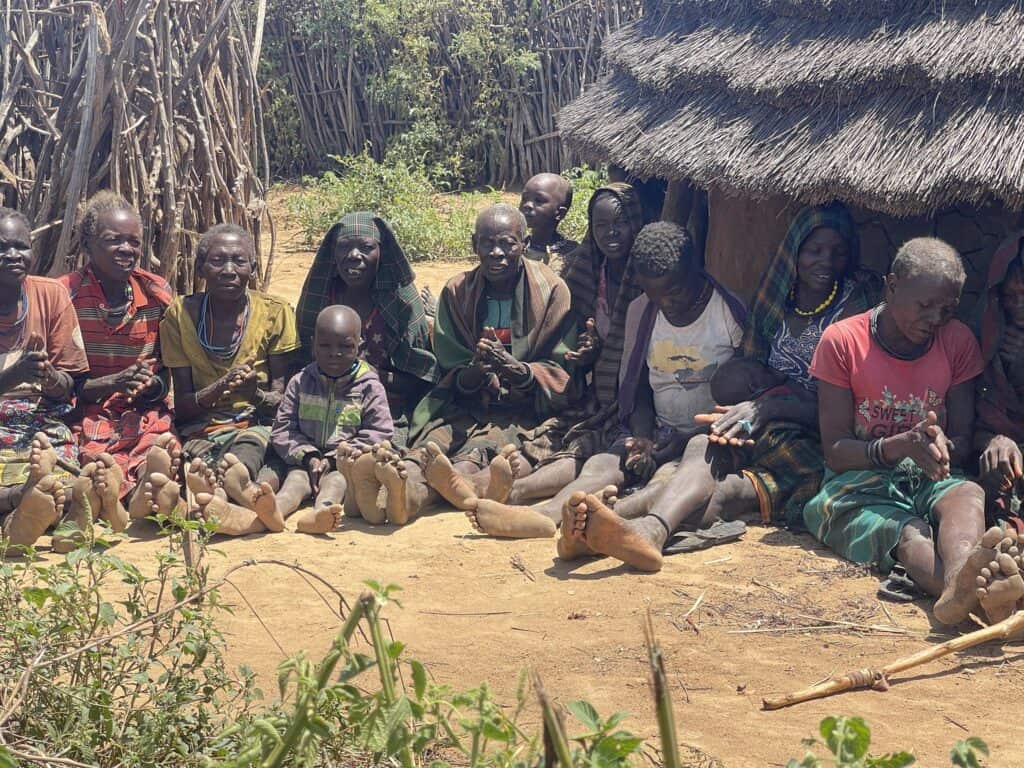 Eine Gruppe von Menschen, möglicherweise aus einer indigenen Gemeinschaft in Afrika, sitzt zusammen auf dem Boden.