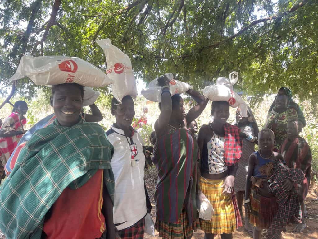 Menschen tragen Taschen mit Nahrungsmittelhilfe unter einem Baum.