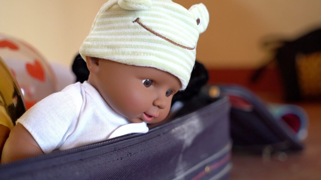 Entzückende schwarze Babypuppe mit Froschhut, die aus einer Tasche herausschaut.