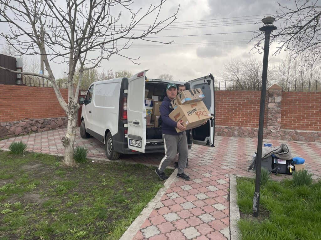 Zwei Männer laden Kisten mit humanitärer Hilfe aus einem Lieferwagen aus.