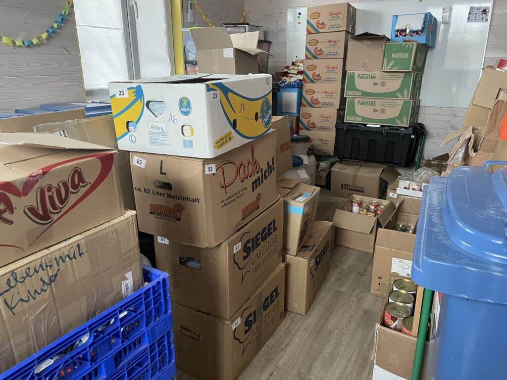 Ein Lagerraum voller Kisten mit Lebensmittelspenden. Zu sehen sind Kisten mit den Aufschriften „Nestle“, „Magic“ und „Viva“.