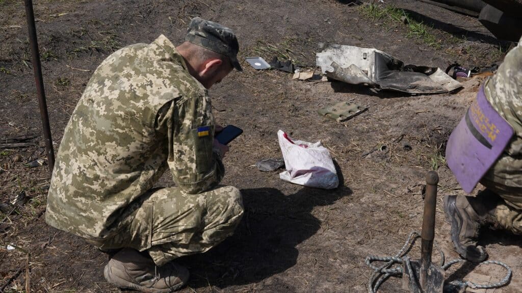 Ein ukrainischer Soldat untersucht mithilfe eines Smartphones Beweise in der Nähe eines beschädigten Fahrzeugs.