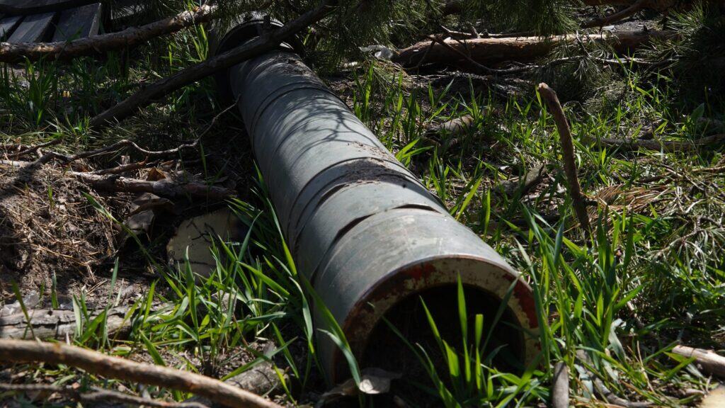 Großes Metallrohr mit Ästen in einer Grasfläche entsorgt.