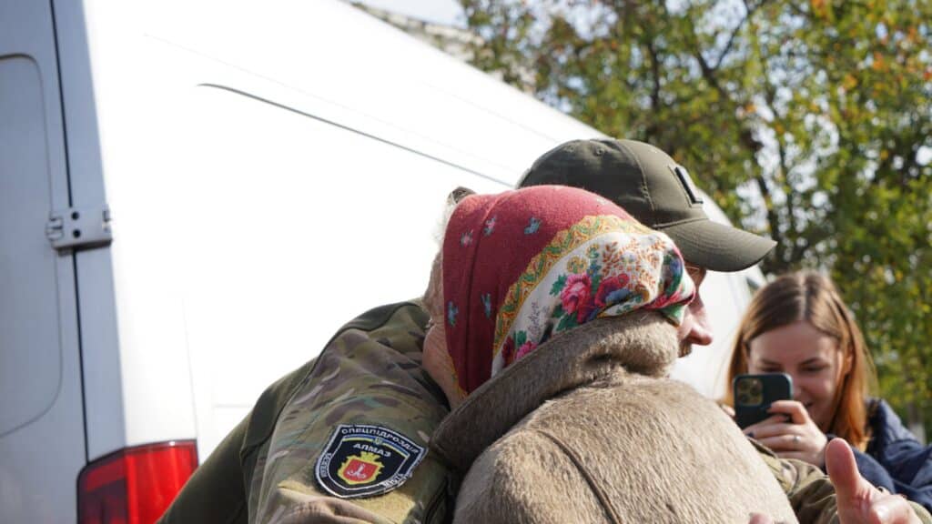 Ukrainischer Soldat tröstet ältere Frau, Aufnäher der Spezialeinheit Almaz sichtbar.