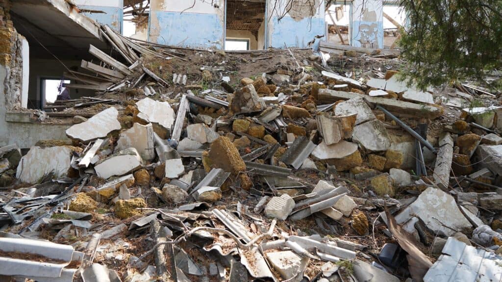 Trümmer eines eingestürzten Gebäudes mit zerbrochenem Beton, Holz und Dachmaterialien.