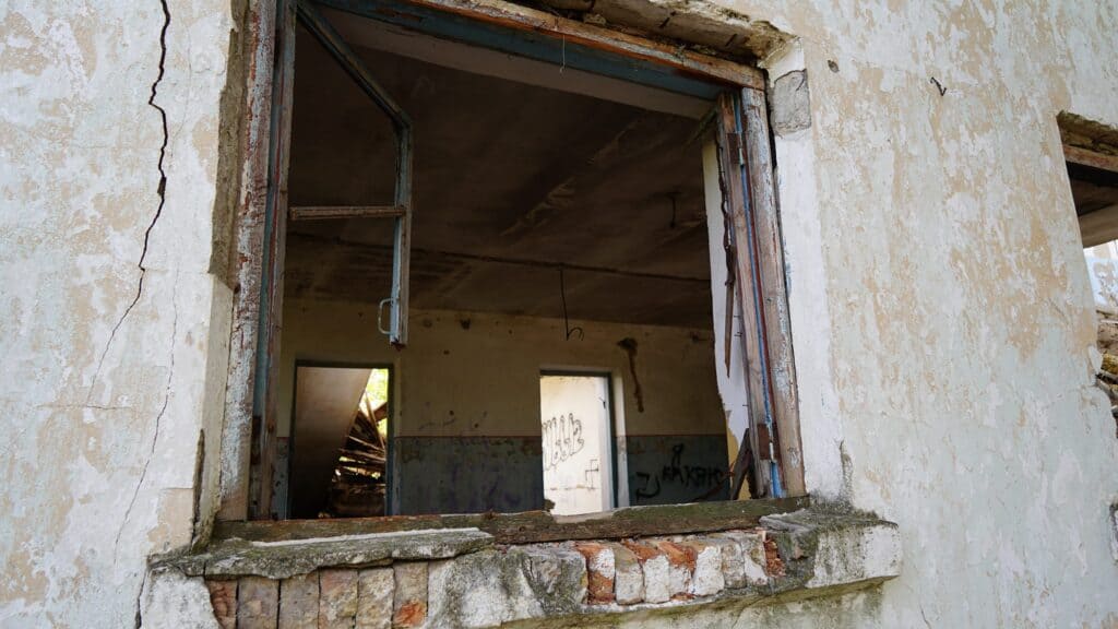 Zerstörtes Gebäudefenster mit zerbrochenem Glas und Graffiti im Inneren