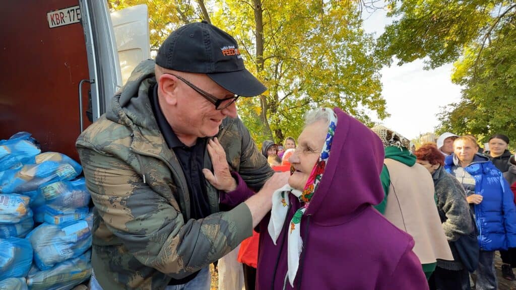 Mann in Tarnjacke reicht einer älteren Frau in der Schlange für humanitäre Hilfe Essen.