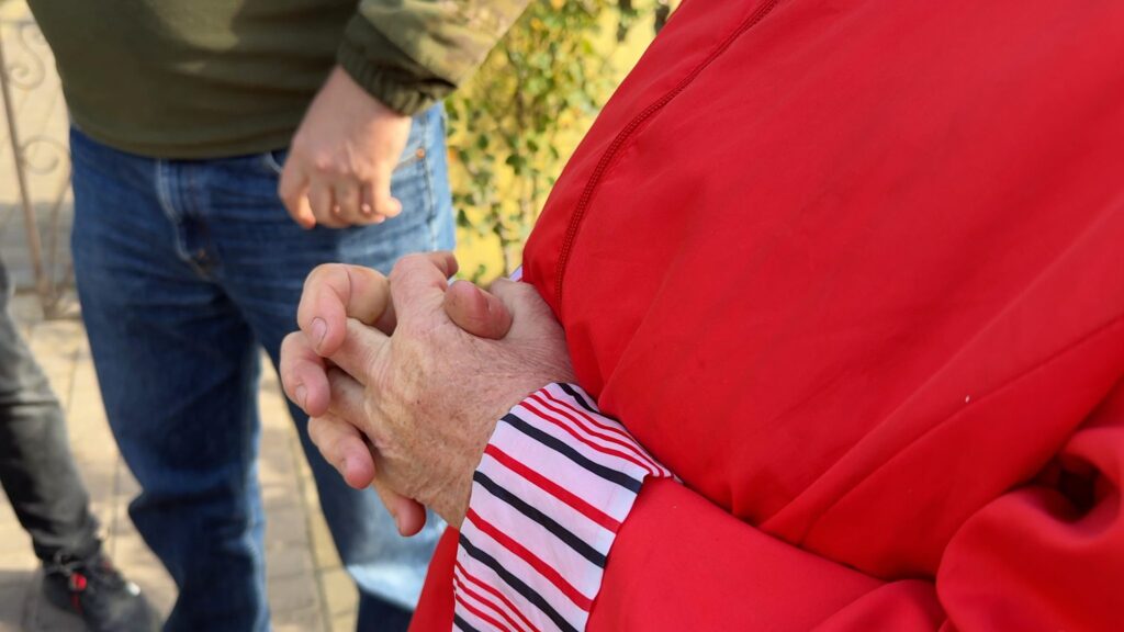 Nahaufnahme gefalteter Hände; Person trägt eine rote Jacke mit gestreiften Manschetten.