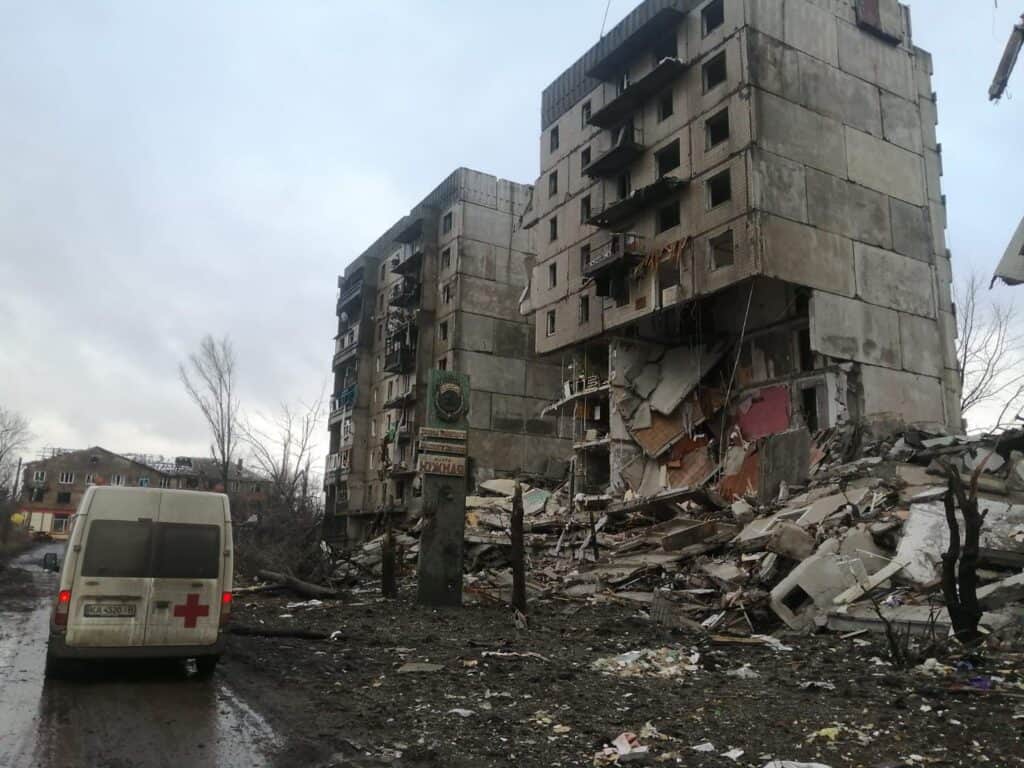 Zerstörte Wohnhäuser in der Ukraine, ein Krankenwagen parkt in der Nähe.