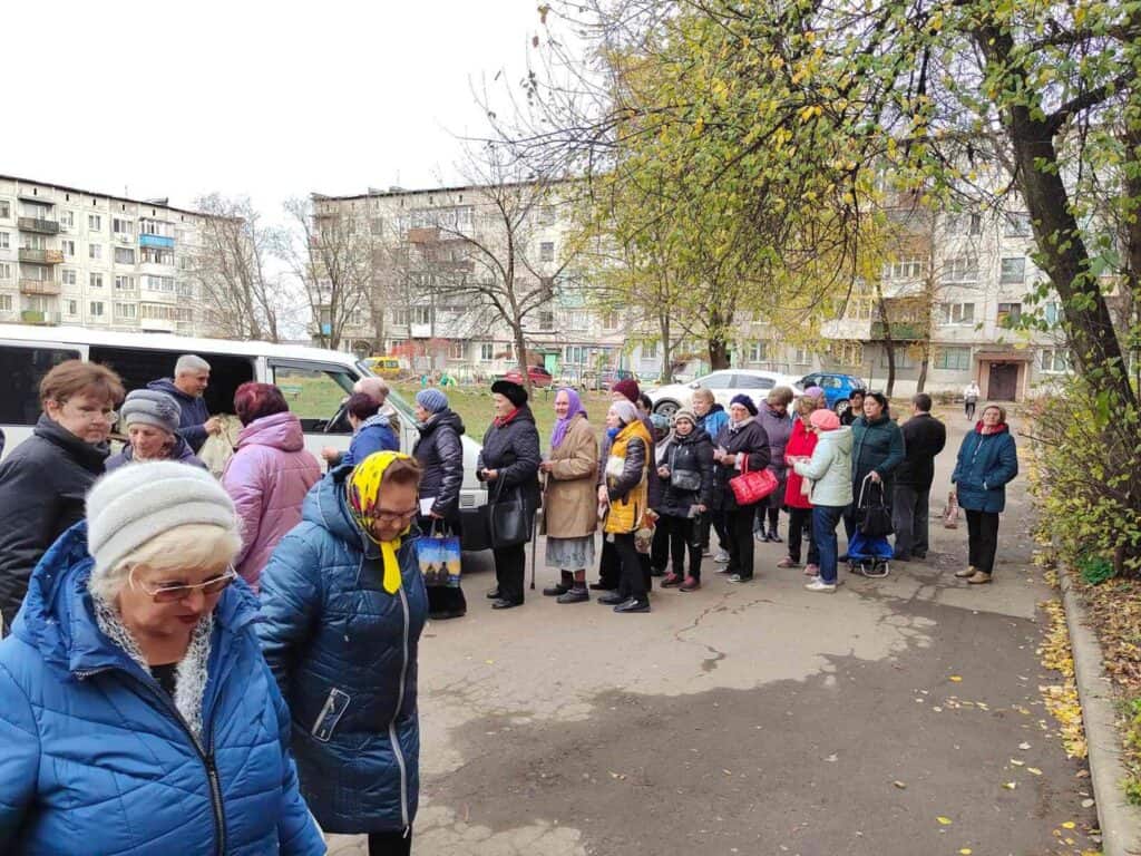 Eine lange Schlange älterer Menschen wartet draußen auf Hilfe oder eine Dienstleistung.