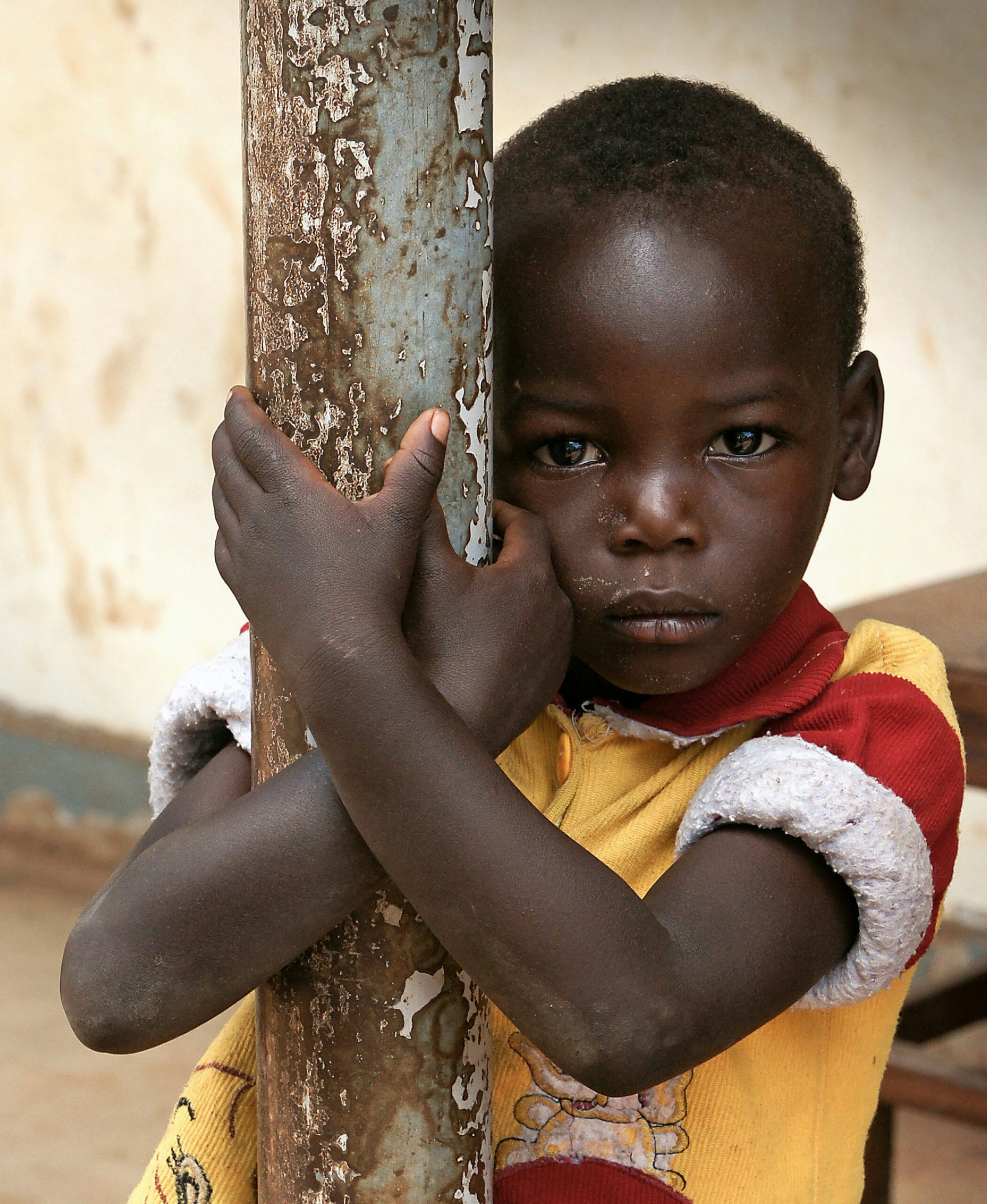 Junges afrikanisches Kind umarmt einen verwitterten Pfosten, ernster Gesichtsausdruck.