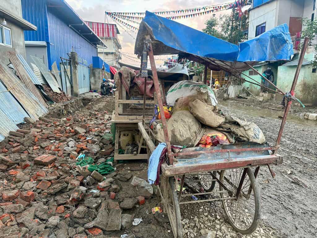 Schlammige Straßenszene nach einer Überschwemmung. Zu sehen ist ein mit geborgenen Gütern und Schutt beladener Karren.