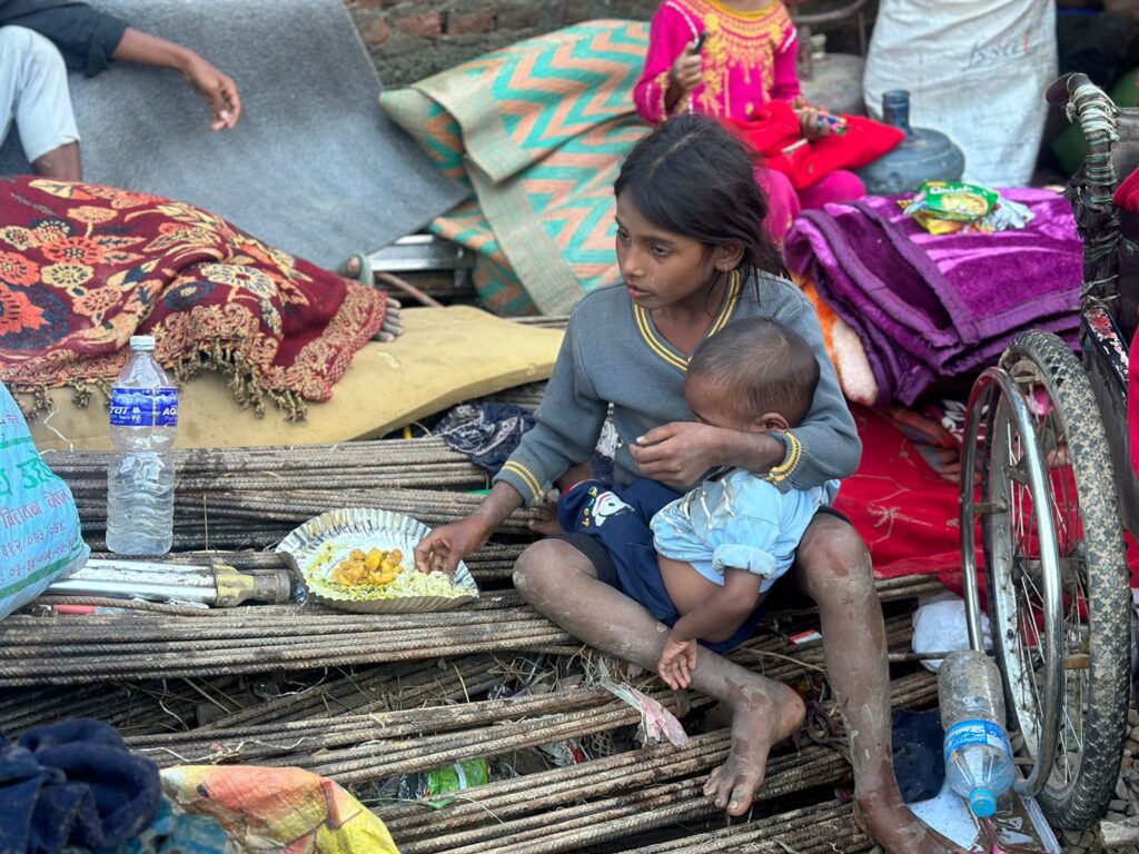 Junges Mädchen hält ein Baby und isst inmitten von Trümmern. Armut, Vertreibung, humanitäre Hilfe.