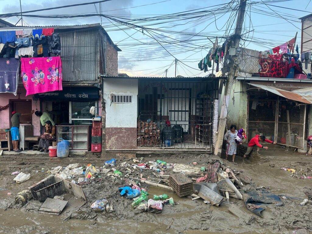 Schlammige Straßenszene in Nepal nach einer Überschwemmung, Trümmer und Anwohner beim Aufräumen.