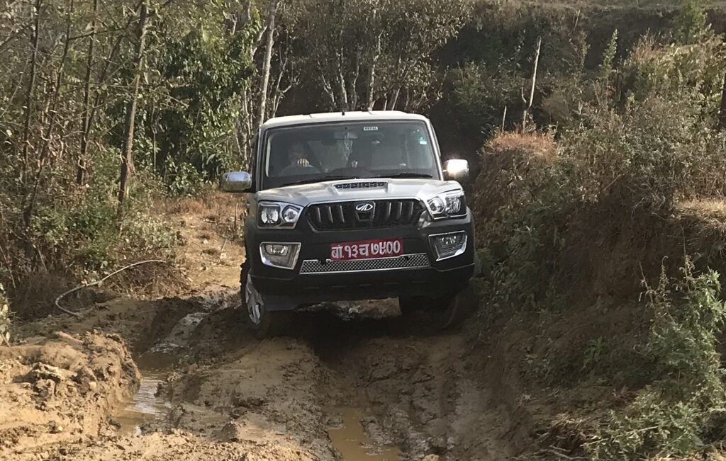 Silberner Mahindra Thar SUV navigiert über schlammigen Offroad-Pfad.