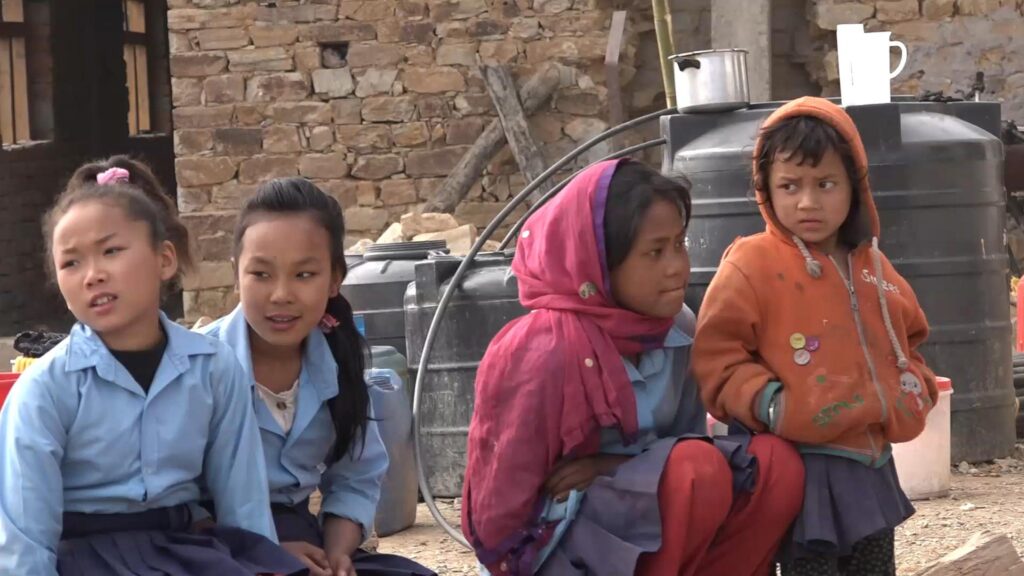 Vier Schulmädchen in Nepal, zwei in Uniform, eine mit rosa Kopftuch und eine in orangefarbener Jacke.