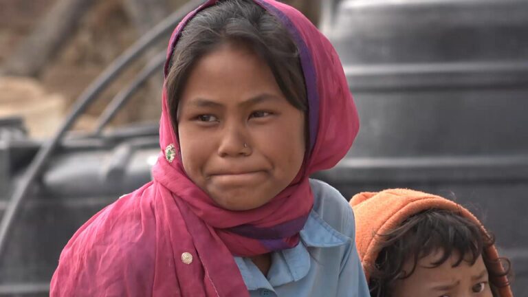 Junges Mädchen mit rosa Kopftuch, möglicherweise aus Nepal, blickt nachdenklich in die Kamera.