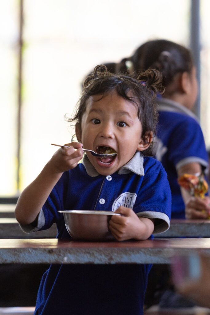 Glückliches Kind in blauer Uniform genießt eine Mahlzeit in der Schule.