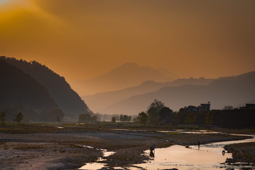 Sonnenuntergang über einem ruhigen Flusstal in Nepal, mit Menschen in der Nähe des Wassers.